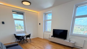 A modern living room with a sofa, a dining table with chairs, a TV, and large windows. - Apartment No.07 with one bedroom (Badenweiler)