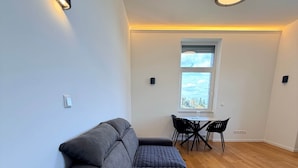 A modern living room with a sectional sofa, a dining area with a table and chairs, and a large window with a view. - Apartment No.07 with one bedroom (Badenweiler)