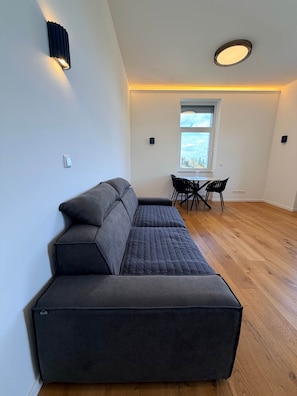 Ein modernes Wohnzimmer mit einer Eckcouch, einem Essbereich mit Tisch und Stühlen sowie einem großen Fenster mit Blick.