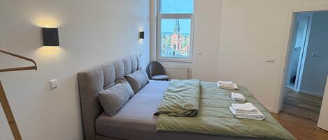 A modern bedroom with a large bed, a view of a church through a window, and a staircase.