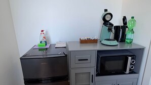 Een compacte kitchenette met een zwarte koelkast, een magnetron, een kleine oven en een koffiezetapparaat.