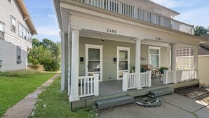 A two-story house with a porch, numbered 2406 and 2404, featuring a small outdoor seating area with chairs and a table. - The Maple Attic – Bright 3BR Retreat Near Downtown (Saint Joseph)