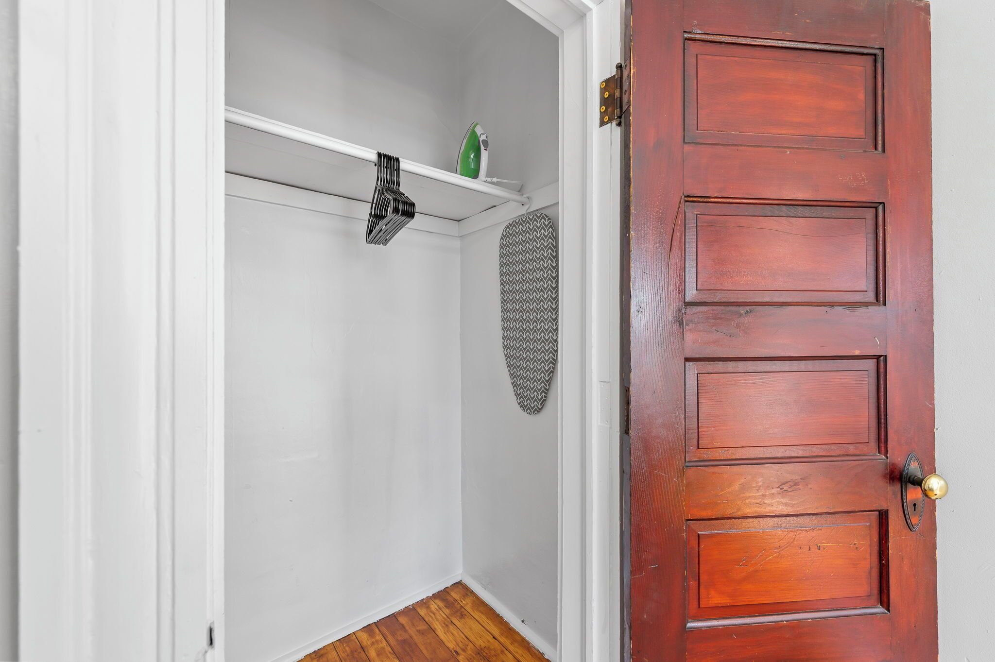 A closed wooden door with a brass doorknob, a white wall, and a wooden floor.