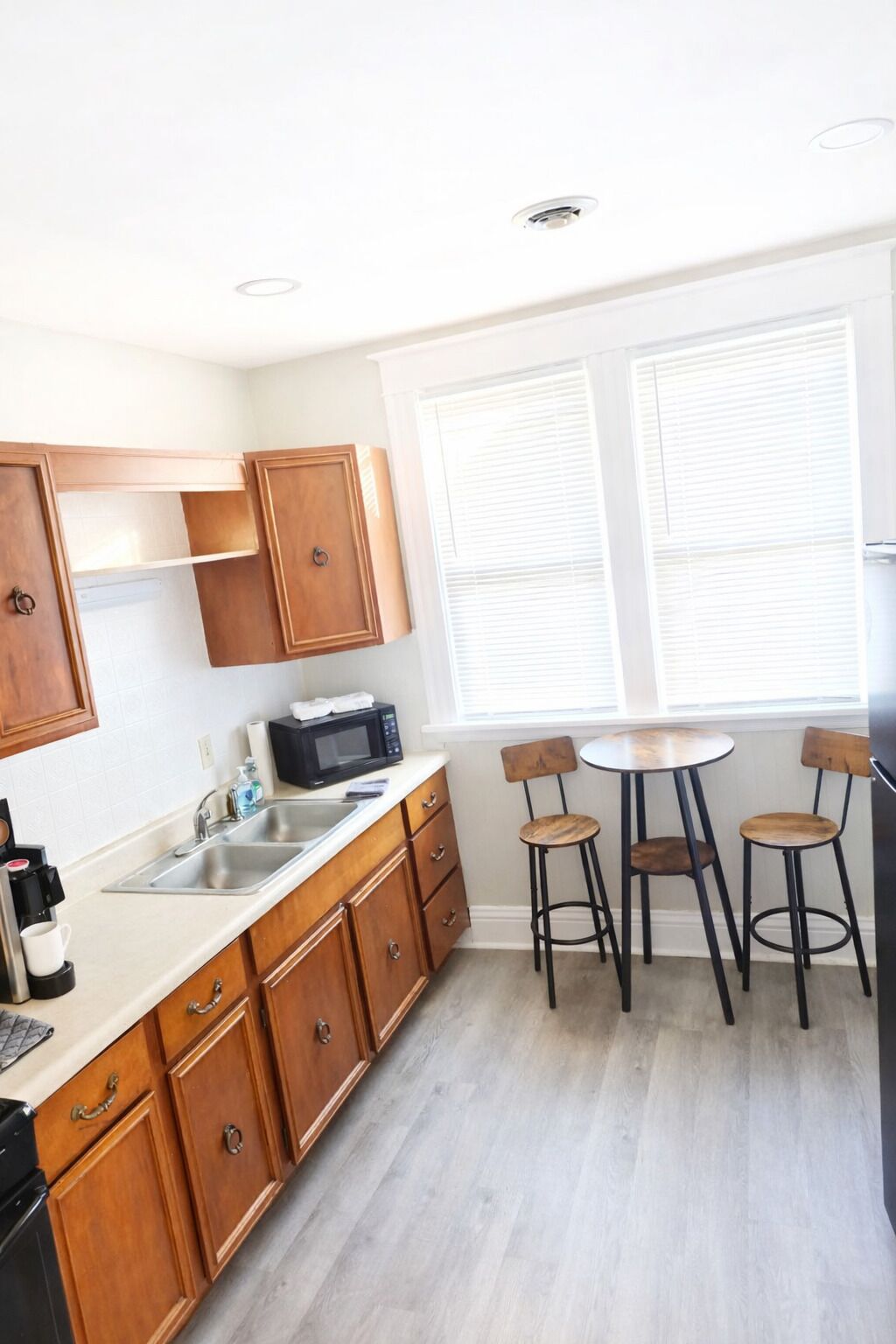 A kitchen with wooden cabinets, a sink, a microwave, and a small dining area with stools.