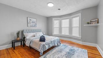 A bedroom with a bed, a nightstand, a window with blinds, and a ceiling light.