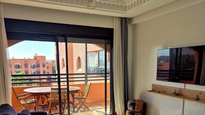 A living room with a sofa set, a small round table, and a balcony with a view of buildings. - Comfortable poolside apartment near the medina (Marrakesh)