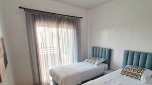 A hotel room with two beds, a large window with curtains, and a chandelier. - Comfortable poolside apartment near the medina (Marrakesh)