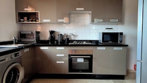 A modern kitchen with a washing machine, microwave, oven, and a hanging light fixture. - Comfortable poolside apartment near the medina (Marrakesh)