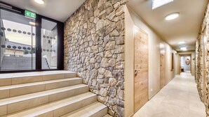 Un couloir d’hôtel aux murs en pierre, aux portes en bois et à l’escalier menant à un étage supérieur.