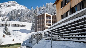Un bâtiment moderne avec une façade en bois, une piste de ski en arrière-plan et des arbres couverts de neige.