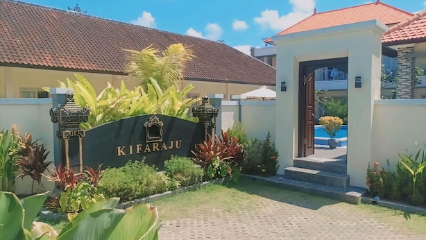 Ein Hotel Eingang mit einem Schild mit der Aufschrift 'KIFARAJU', umgeben von tropischen Pflanzen und einem Ziegeldach.