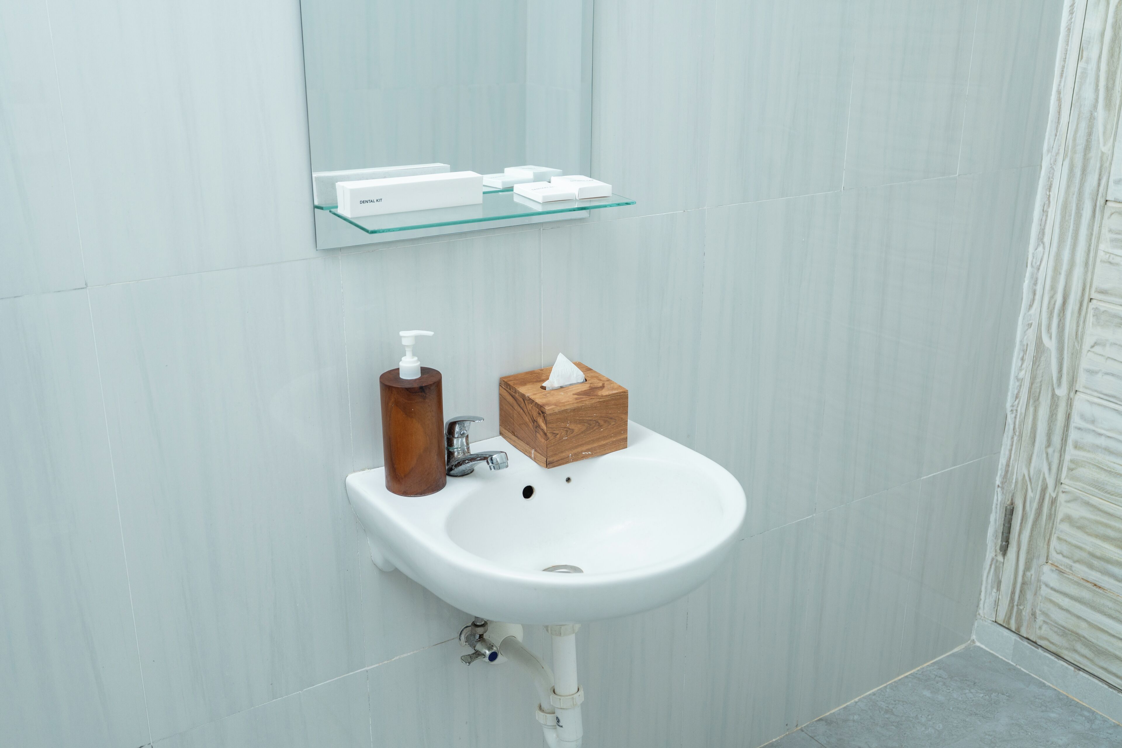 A bathroom with a white sink, a wooden box, and a glass shelf with toiletries.