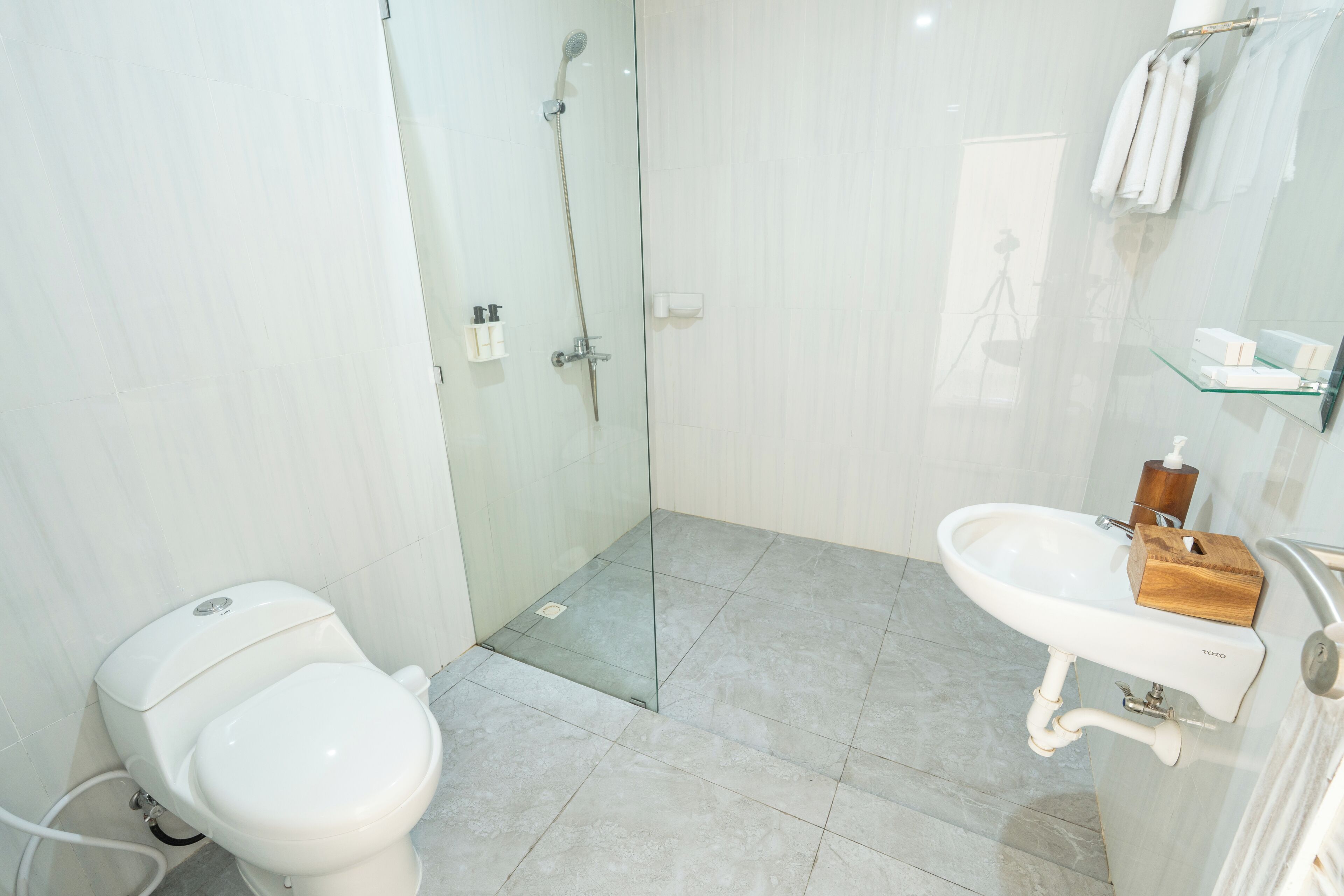 A modern bathroom with a glass shower enclosure, a white toilet, and a sink with a wooden soap holder.