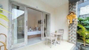 Ein Zimmer mit einem Bett, einem kleinen Tisch und Stühlen. Eine Schiebetür aus Glas führt in einen anderen Raum.