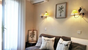A cozy living room with a sofa, two wall-mounted lamps, a framed plant, and a small table with a vase. - Le Petit Bonheur - Studio with sea view - Côte d'Azur (Roquebrune-sur-Argens)
