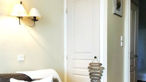 A cozy room with a dark-colored sofa, a wall-mounted lamp, and a door with a sign hanging on it. - Le Petit Bonheur - Studio with sea view - Côte d'Azur (Roquebrune-sur-Argens)