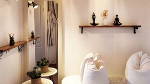 A cozy bedroom with a white fluffy bed, a small round table with potted plants, a mirror with wall-mounted lights, and a shelf with decorative items. - Le Petit Bonheur - Studio with sea view - Côte d'Azur (Roquebrune-sur-Argens)