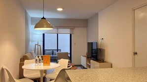Una habitación moderna y bien iluminada con una mesa de comedor, sillas, televisor y una kitchenette.