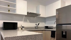 Una cocina moderna con armarios blancos, un refrigerador de acero inoxidable, un microondas y encimeras de granito.