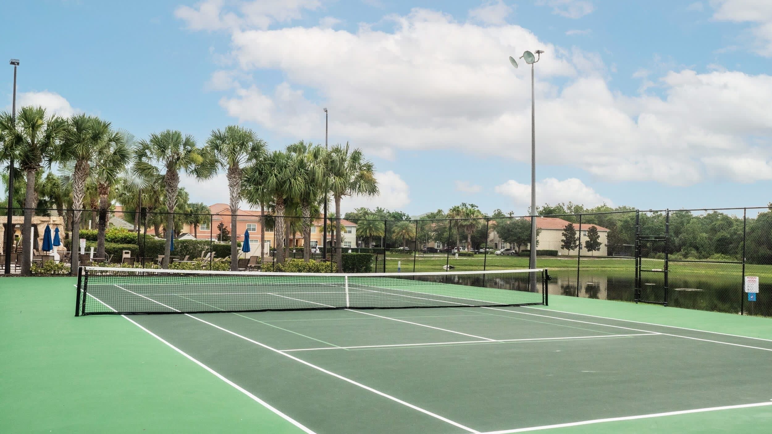 Un court de tennis avec un filet, entouré de palmiers et d’une clôture.
