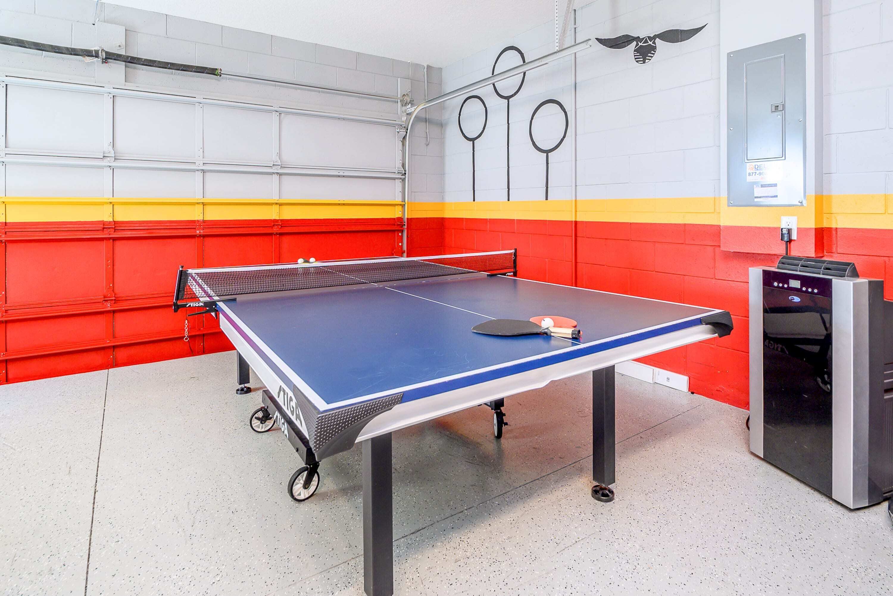 A ping pong table in a room with red and yellow walls, a metal rack, and a control panel.