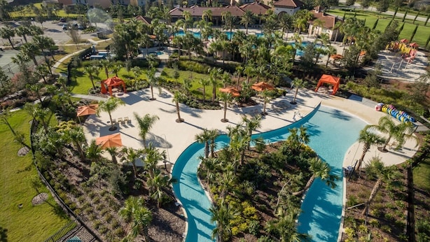Un complexe hôtelier doté d’une grande piscine, de palmiers et offrant une vue sur les maisons environnantes.