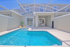 A swimming pool with a glass ceiling, a patio area with a table and chairs, and a view of the house in the background. - Upstay - Championsgate Home w Private Pool BBQ (Davenport)