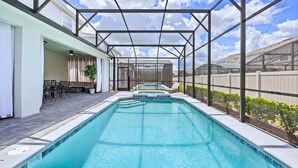 Ein rechteckiger Swimmingpool mit Glasabdeckung, umgeben von einer Terrasse mit Gartenmöbeln und Blick auf eine Wohngegend.