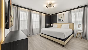 A modern bedroom with a large bed, a TV mounted on the wall, and a small table by the window. - Exquisite 10br Luxury Villa Pool Hot Tub Arcade (Davenport)