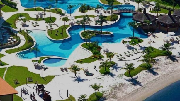 Vue aérienne d’un complexe hôtelier doté de plusieurs piscines, de chaises longues et de palmiers.