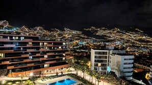 Ein modernes Hotel mit Schwimmbad, mehreren Balkonen und Blick auf die nächtliche Stadt.