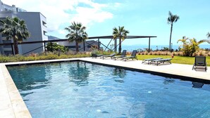 Ein Swimmingpool mit Liegestühlen, Palmen und Blick auf den Ozean.
