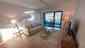 Ein modernes Wohnzimmer mit einer Couch, einem Couchtisch und Lampen. Ein großes Fenster bietet Blick auf eine Stadtlandschaft.