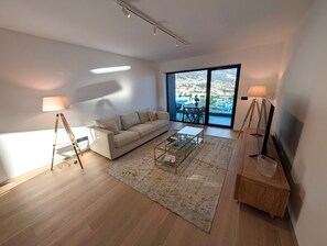 Un salon moderne avec un canapé, une table basse et des lampes. Une grande fenêtre offre une vue sur le paysage urbain.