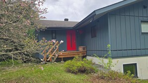 Una casa de dos pisos con una puerta roja y una escalera de madera que lleva al porche delantero.