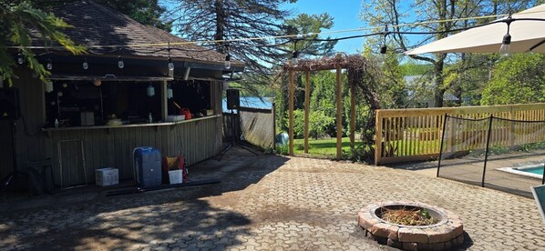 A backyard with a barbecue area, a wooden pergola, a fenced pool area, and a fire pit.