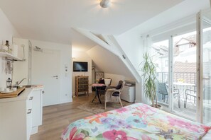 Ein Schlafzimmer mit einem großen Bett, einem Schreibtisch und einem Fernseher. Es gibt einen Balkon mit Blick auf die Umgebung.