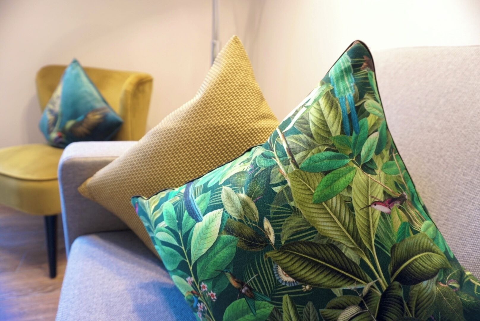 Un canapé agrémenté de deux coussins décoratifs, dont l’un présente un motif de feuilles tropicales et l’autre est d’une couleur unie.