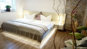 Ein modernes Schlafzimmer mit einem großen Bett, Nachttischen, einer Stehlampe und einer Zimmerpflanze, an einer Ziegelwand.