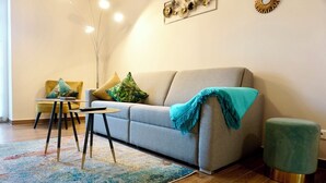 Ein modernes Wohnzimmer mit einer grauen Couch, einem kleinen runden Tisch, einem gelben Sessel und einem türkisfarbenen Ottomanen.
