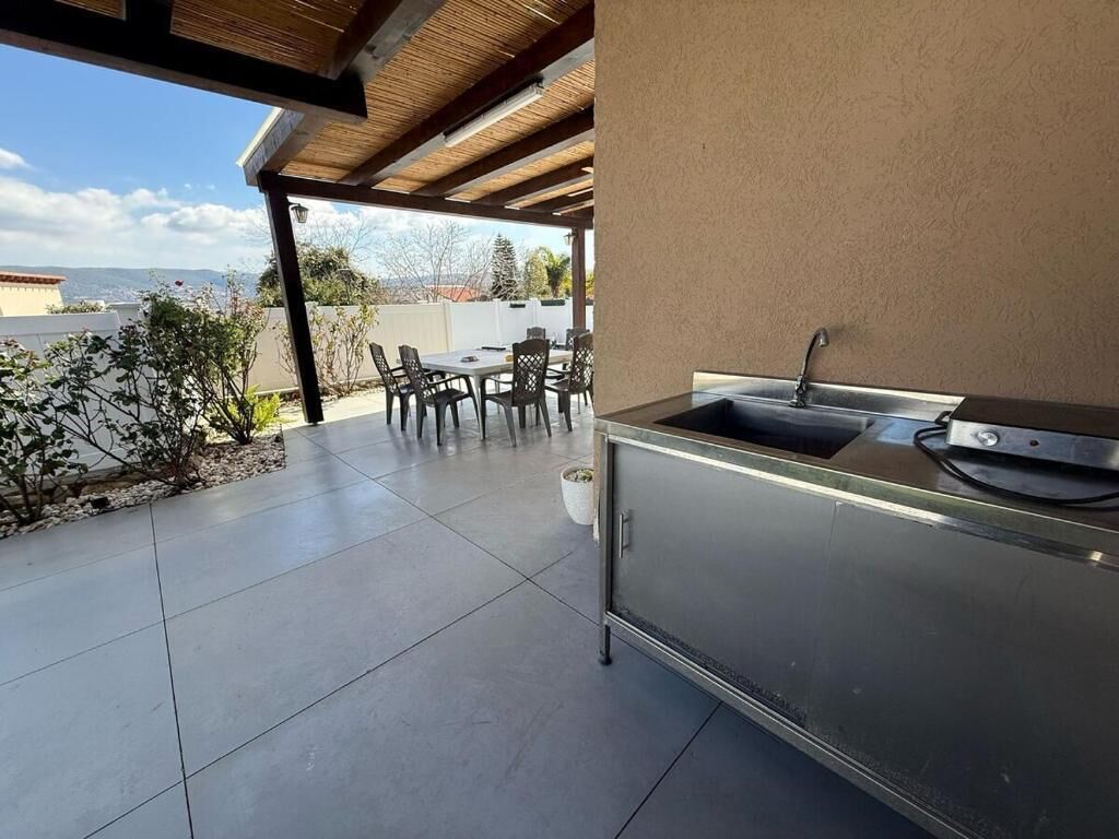 Une cuisine extérieure équipée d’un évier et d’un barbecue, entourée d’une terrasse avec des chaises et offrant une vue sur la ville.
