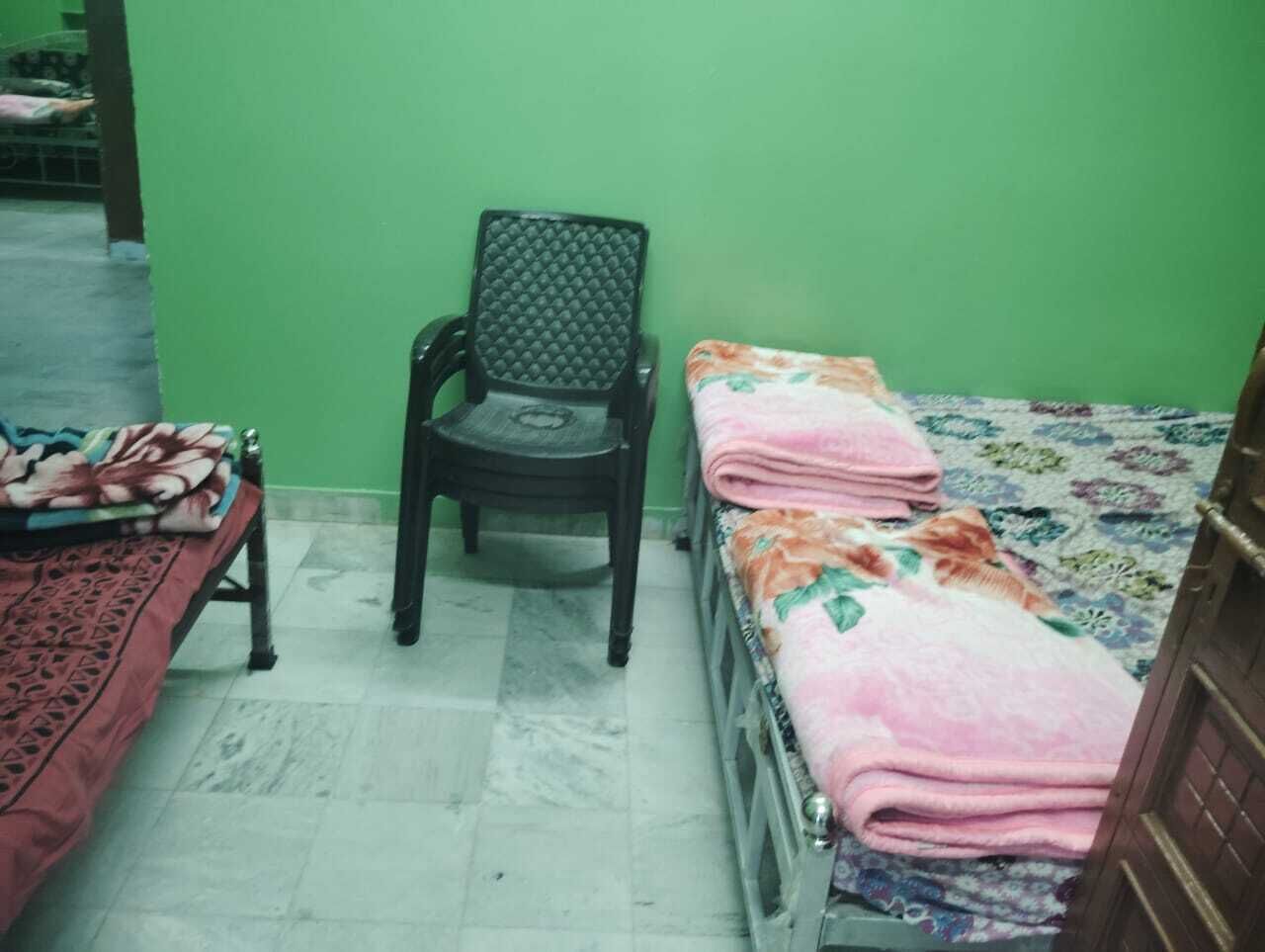 Ein kleines Zimmer mit zwei Betten, einem Sessel und einer grünen Wand.