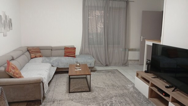A living room with a sofa, a coffee table, a TV, and a window with curtains. - Quiet, spacious apartment in an ideal location (Avignon)