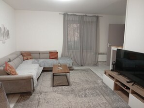 A living room with a sofa, a coffee table, a TV, and a window with curtains. - Quiet, spacious apartment in an ideal location (Avignon)