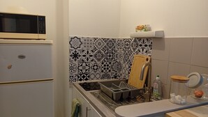 A compact kitchen with a microwave, a sink with a cutting board, and a countertop with a jar and a bottle. - Quiet, spacious apartment in an ideal location (Avignon)