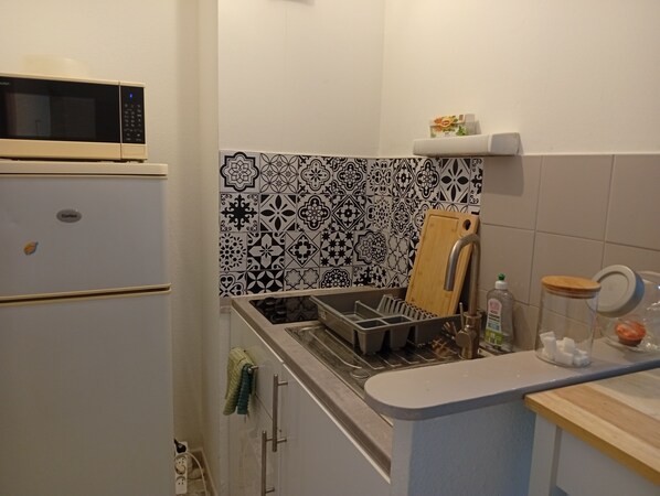 A compact kitchen with a microwave, a sink with a cutting board, and a countertop with a jar and a bottle. - Quiet, spacious apartment in an ideal location (Avignon)