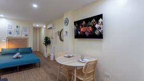 A cozy living room with a sofa, a dining table with chairs, a TV mounted on the wall, and framed pictures on the wall. - Aesthetic Boho Studio • Near Maginhawa & UP (Quezon City)