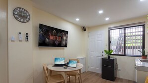 A compact living space with a dining area, a refrigerator, a potted plant, and a large window with bars. - Aesthetic Boho Studio • Near Maginhawa & UP (Quezon City)