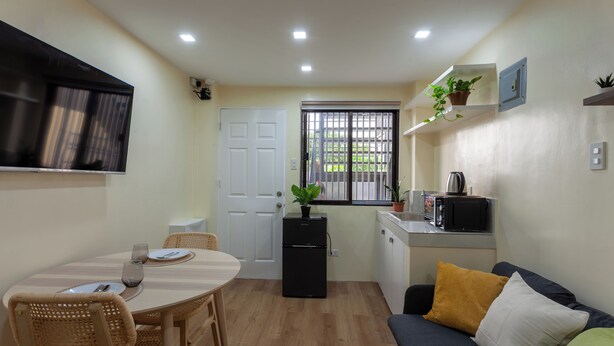 A compact kitchen with a dining area, a refrigerator, a microwave, and a window with a view. - Aesthetic Boho Studio • Near Maginhawa & UP (Quezon City)