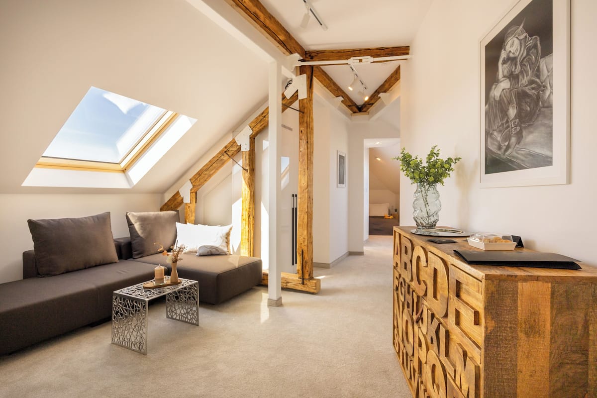 A modern loft apartment with a sloped ceiling, a built-in wooden desk, a sofa, and a skylight.